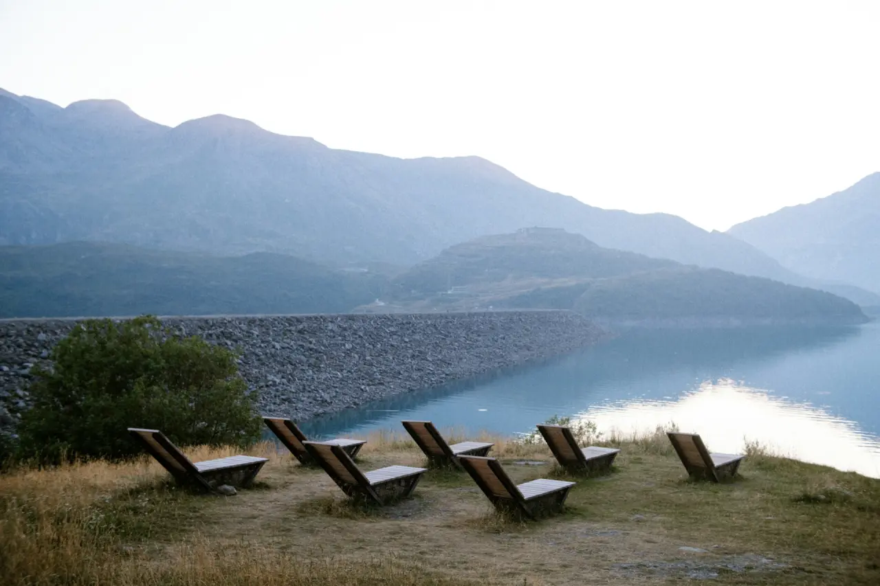 Liegestühle auf einer Wiese mit Blick auf einen Bergsee