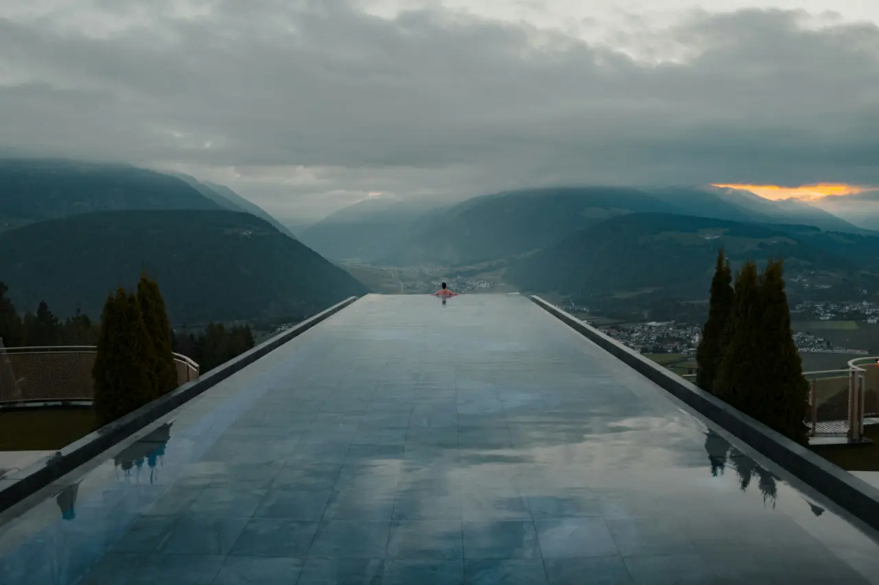 Infinity-Pool mit Blick über ein wolkenverhangenes Alpental