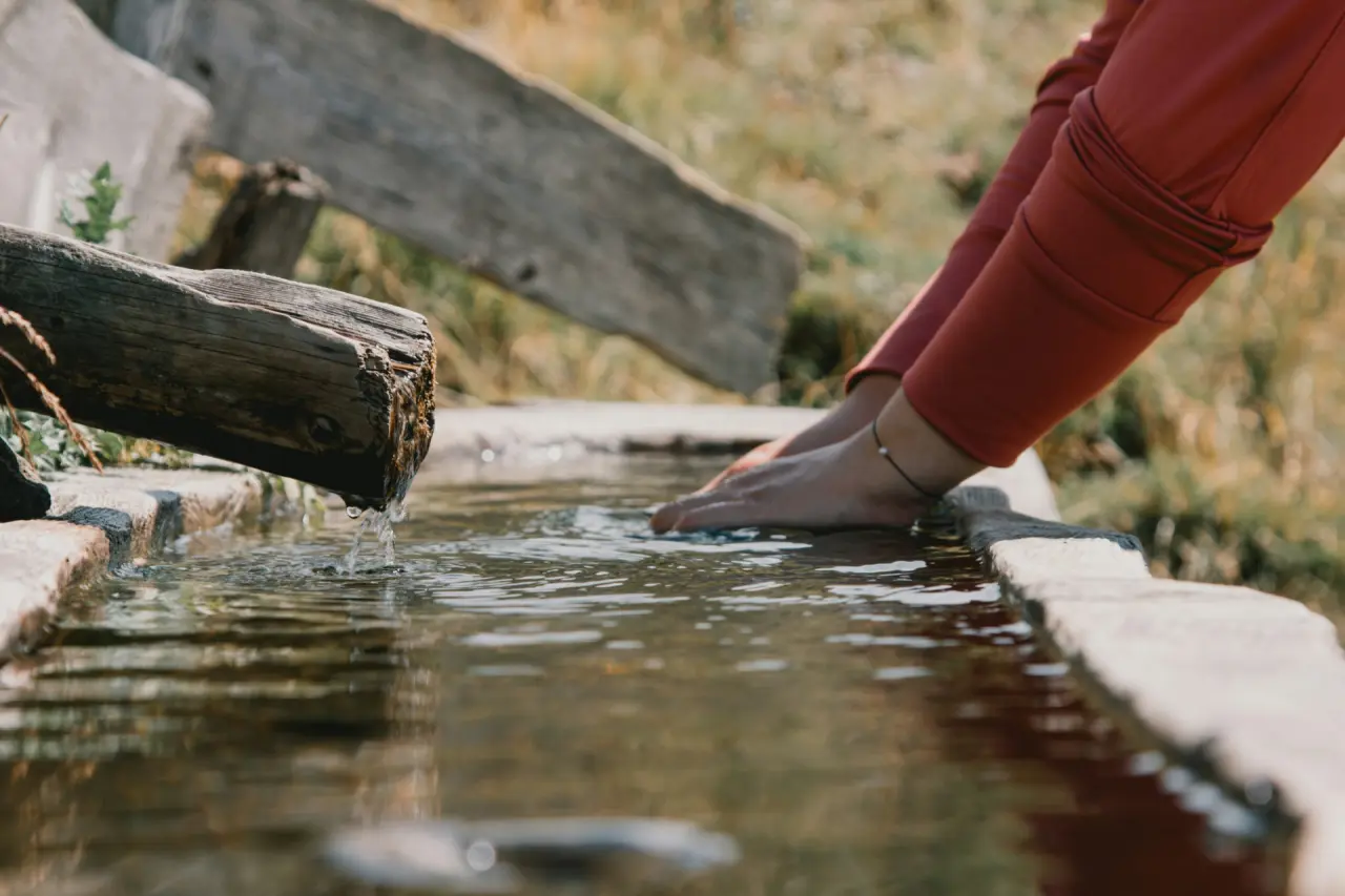 Hände im kalten Wasser eines Kneipp-Armbads mit Holzrand