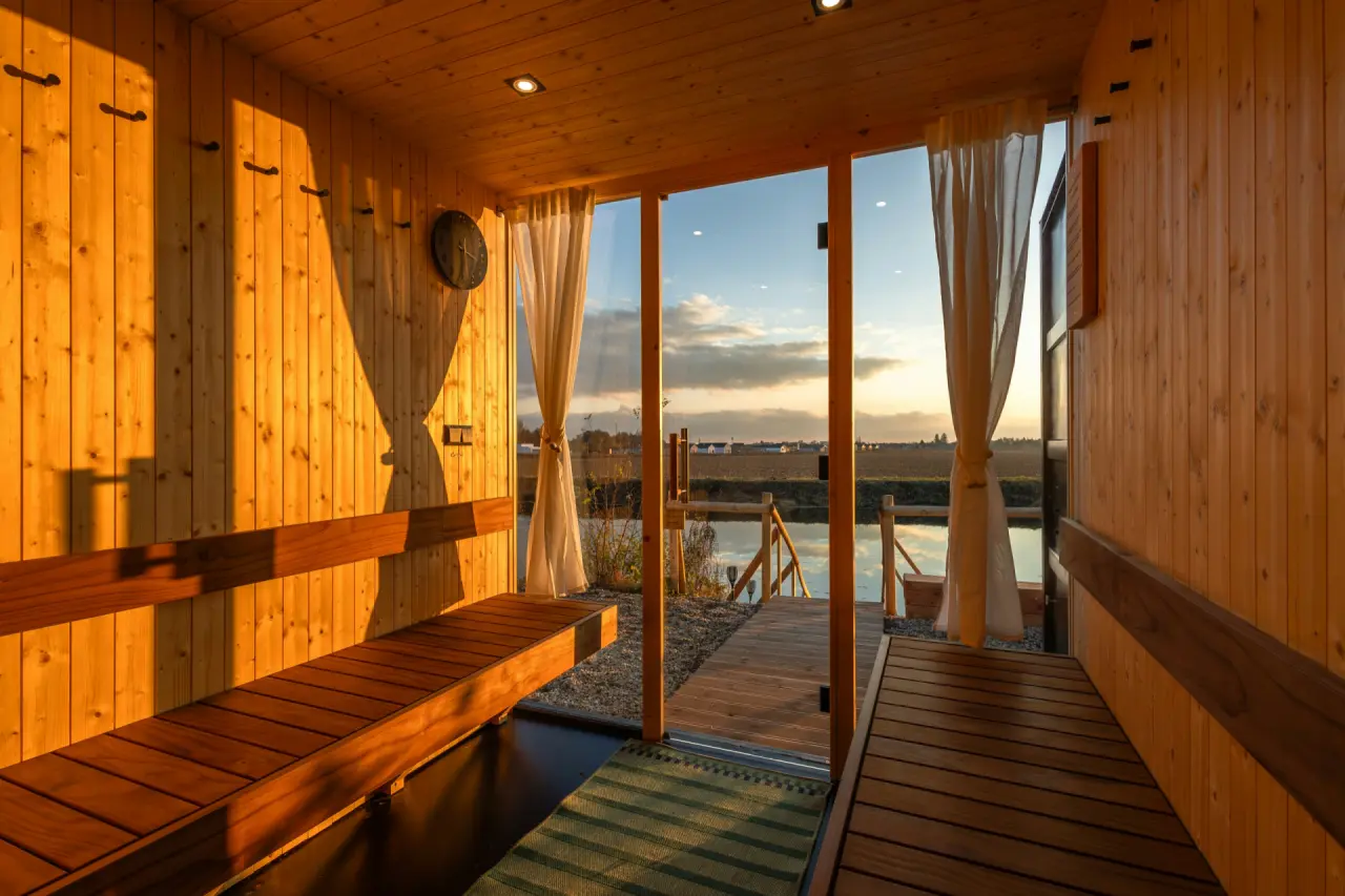 Holzsauna mit offener Tür, Blick über einen Steg auf einen See im Abendlicht