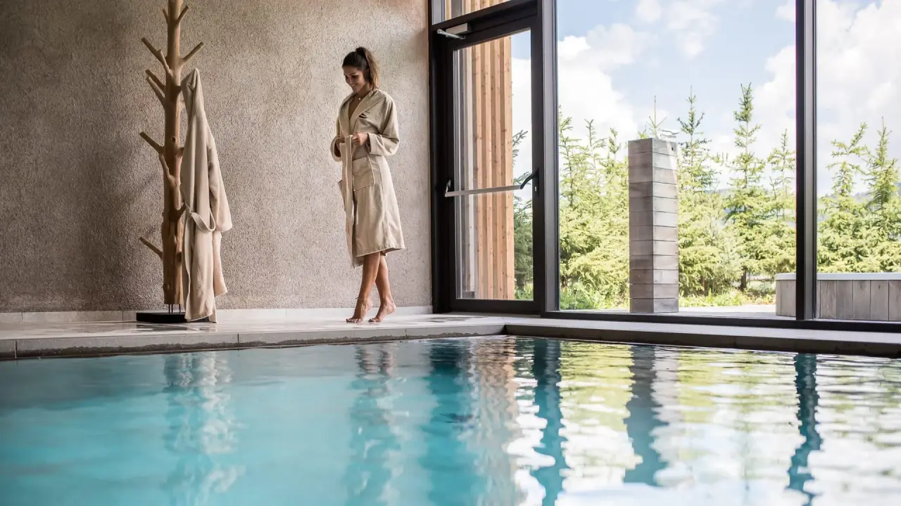 Hotel Restaurant Lëch da Sompunt in La Villa – Frau im Bademantel am Indoorpool mit Waldblick | Wellnesshotel Dolomiten