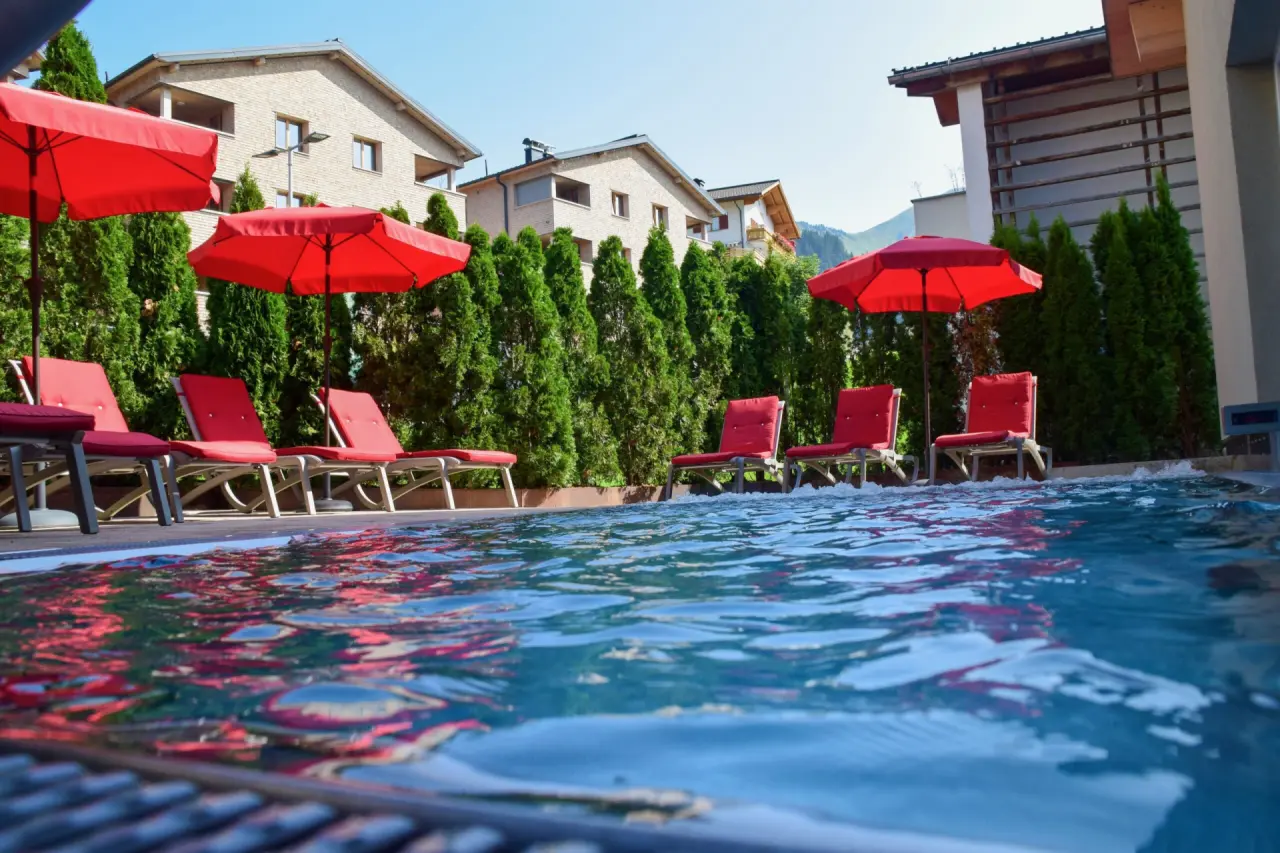 DAS SCHÄFER in Fontanella – Außenpool mit roten Liegen und Sonnenschirmen | Wellnesshotel Vorarlberg