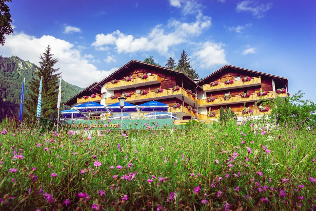 Parkhotel Sonnenhof in Oberammergau – Sommeransicht mit blühender Wiese und Hotel | Wellnesshotel Ammergauer Alpen