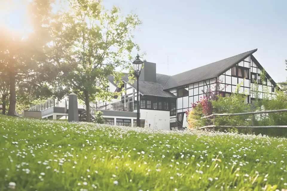 Sporthotel Grafenwald in Daun – Hotelgebäude im Sommer mit grüner Wiese und Bäumen | Wellnesshotel Eifel