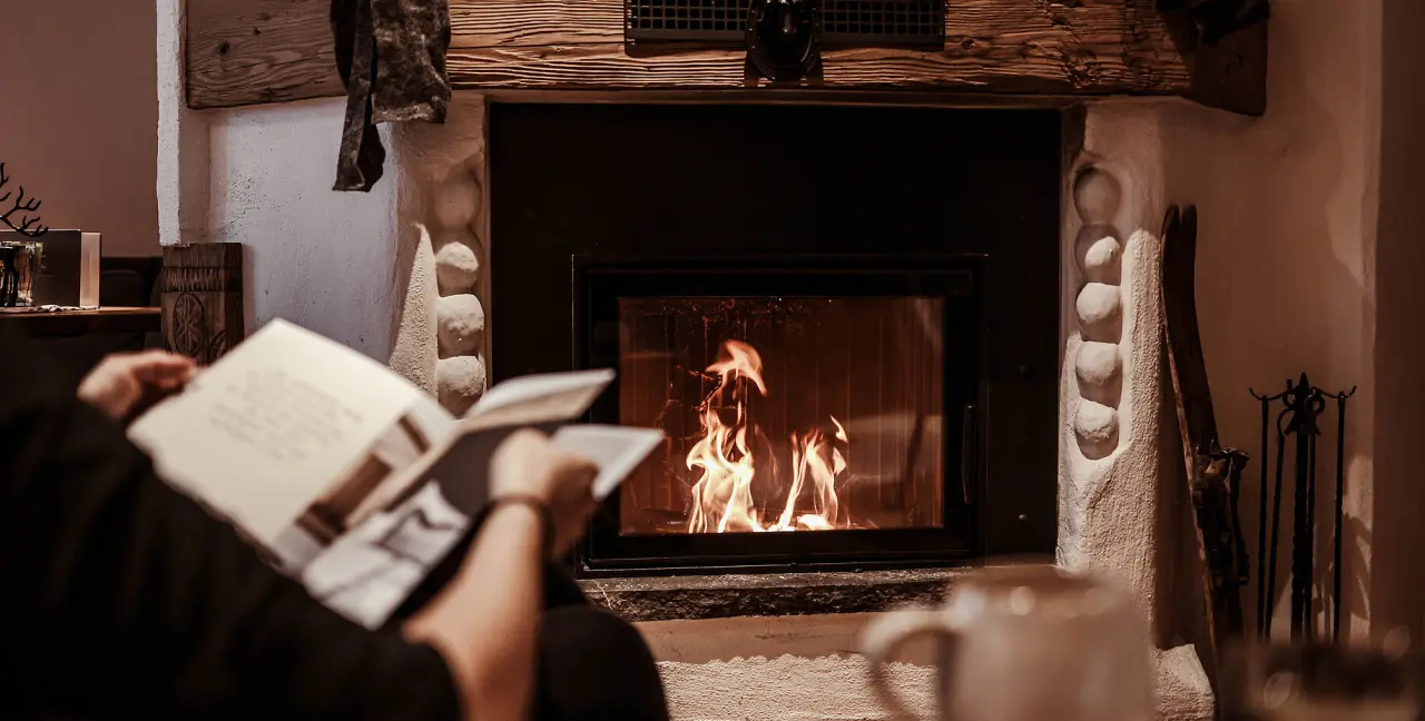 Hotel St. Georg zum See in Maurach – Gemütlicher Kaminbereich mit Feuer und lesender Person | Wellnesshotel Achensee