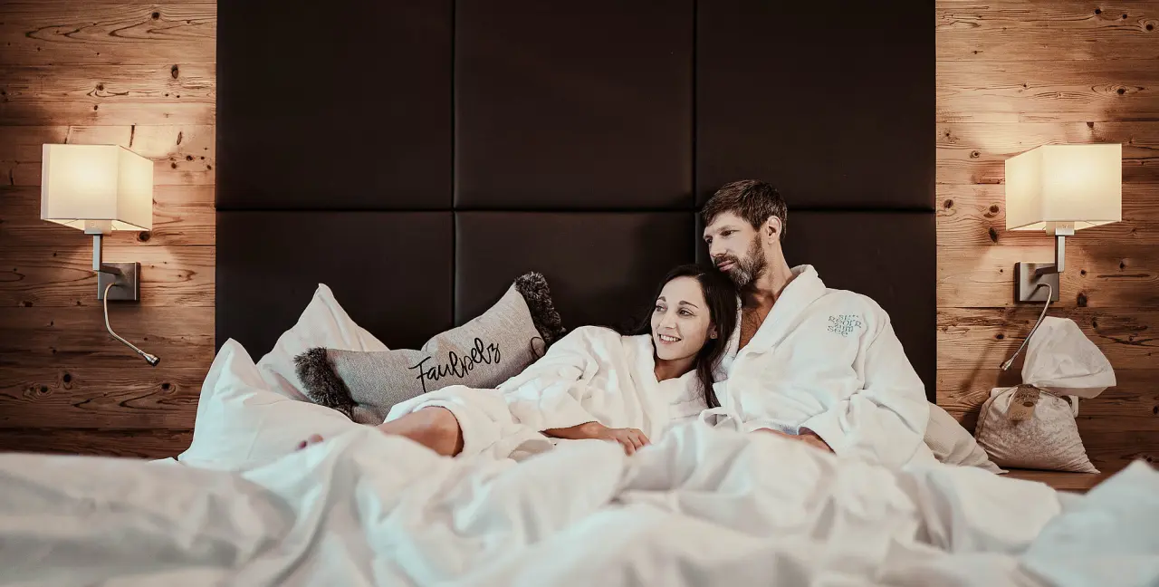 Hotel St. Georg zum See in Maurach – Paar in Bademänteln entspannt im komfortablen Hotelbett | Wellnesshotel Achensee