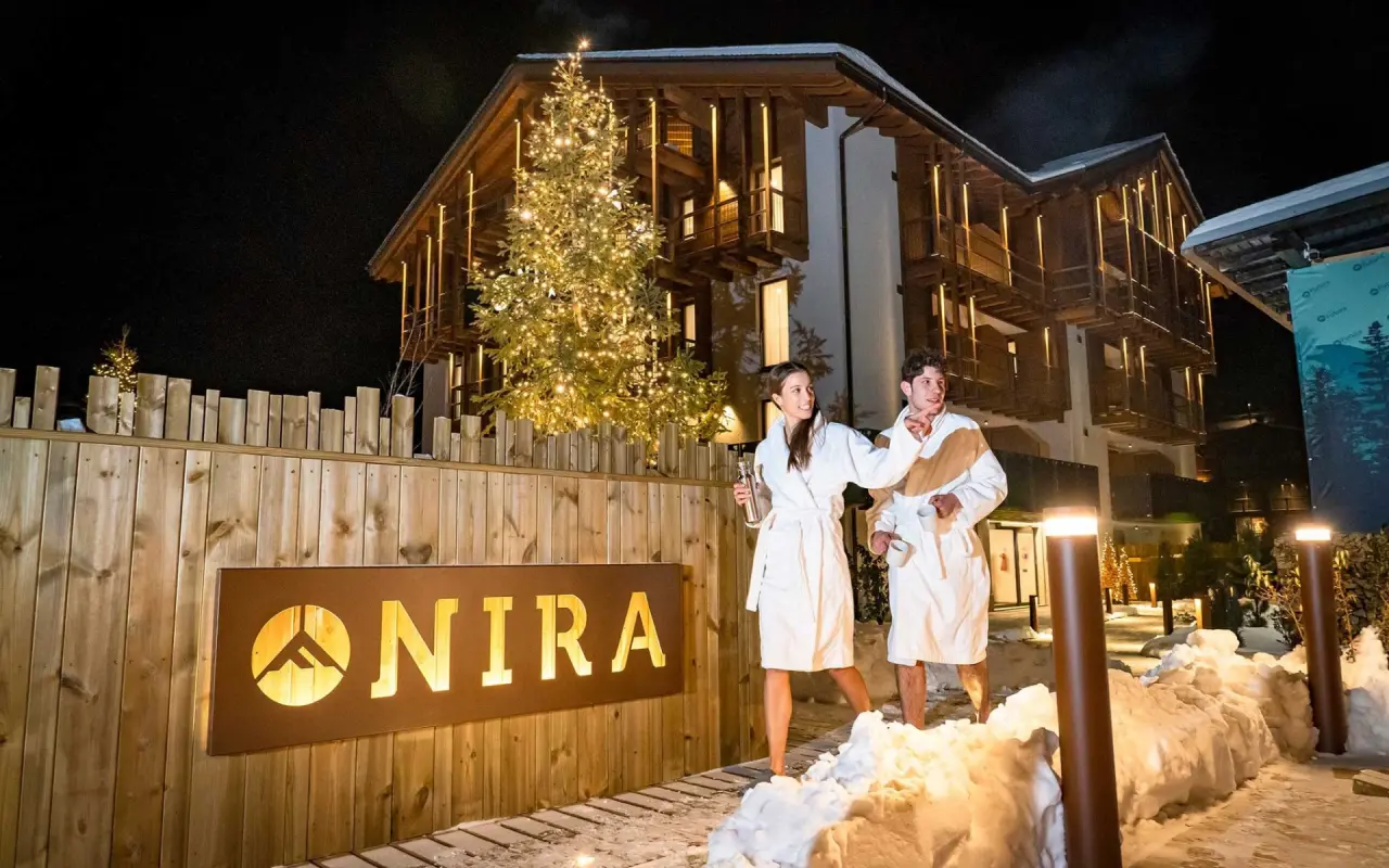 Nira - Mountain Resort Futura in Livigno – Paar in Bademänteln im Schnee vor dem beleuchteten Hotel | Wellnesshotel Italienische Alpen