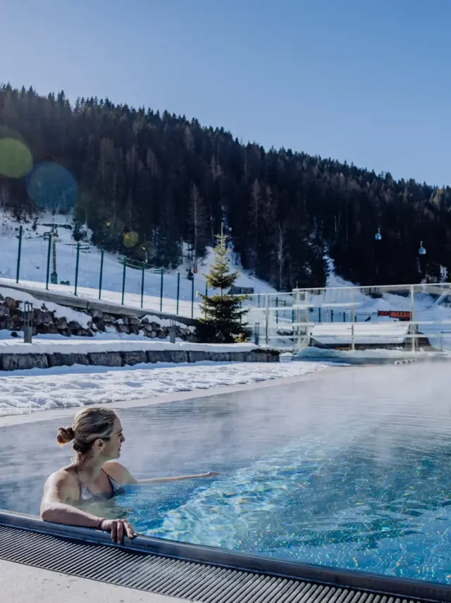Good Life Resort Riederalm in Leogang – Frau entspannt im warmen Außenpool im Winter | Wellnesshotel Salzburger Land