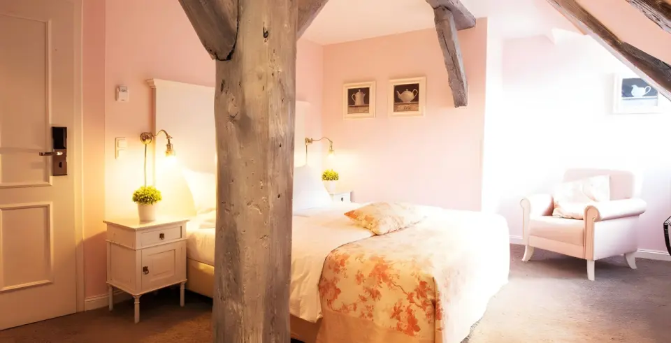 Schloss Basthorst in Crivitz – Gemütliches Hotelzimmer mit Holzbalken und rosa Akzenten | Wellnesshotel Mecklenburg-Vorpommern
