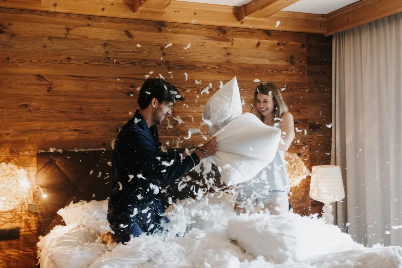 Boutiquehotel Haidachhof in Fügen – Glückliches Paar bei Kissenschlacht im gemütlichen Hotelzimmer | Wellnesshotel Zillertal