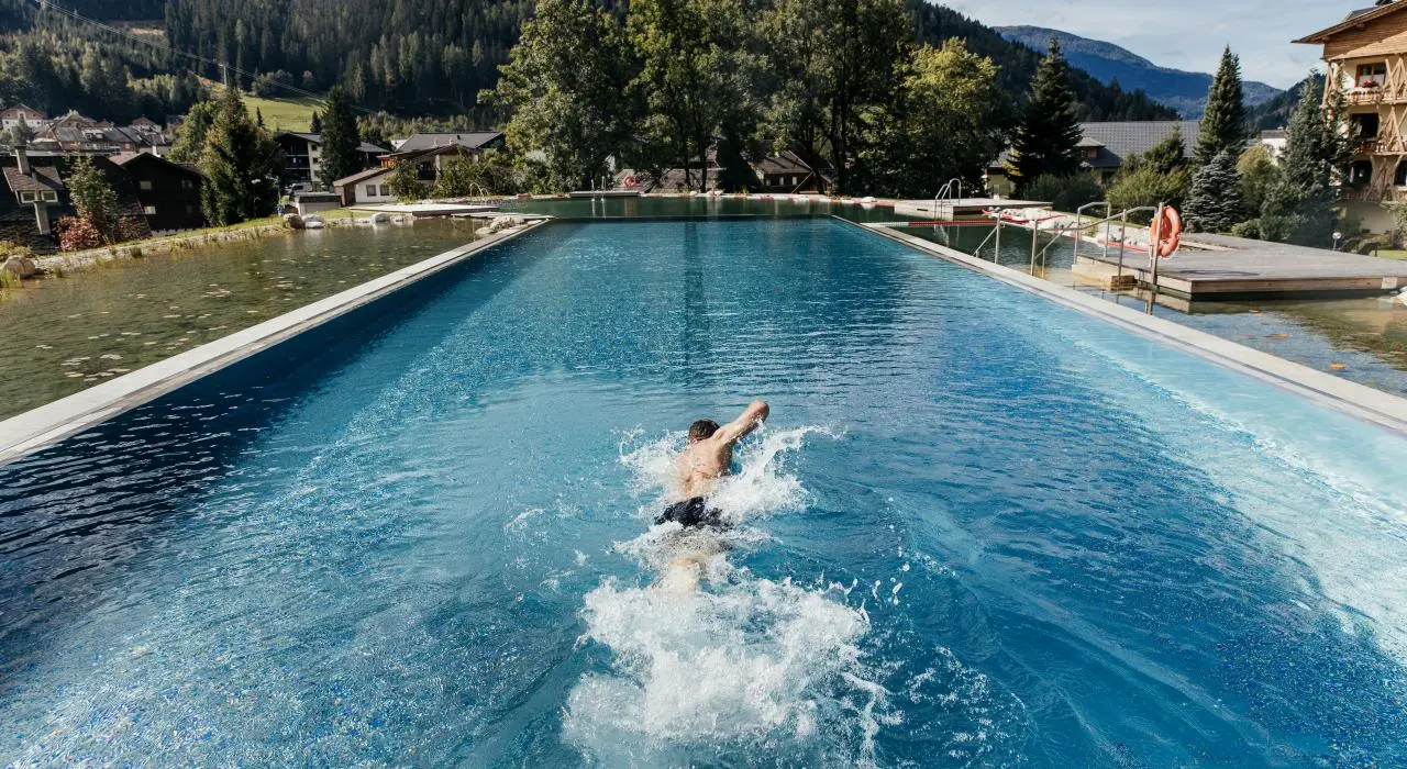 Hotel Pulverer in Bad Kleinkirchheim – Mann schwimmt im großen Außenpool mit Bergblick | Wellnesshotel Kärnten