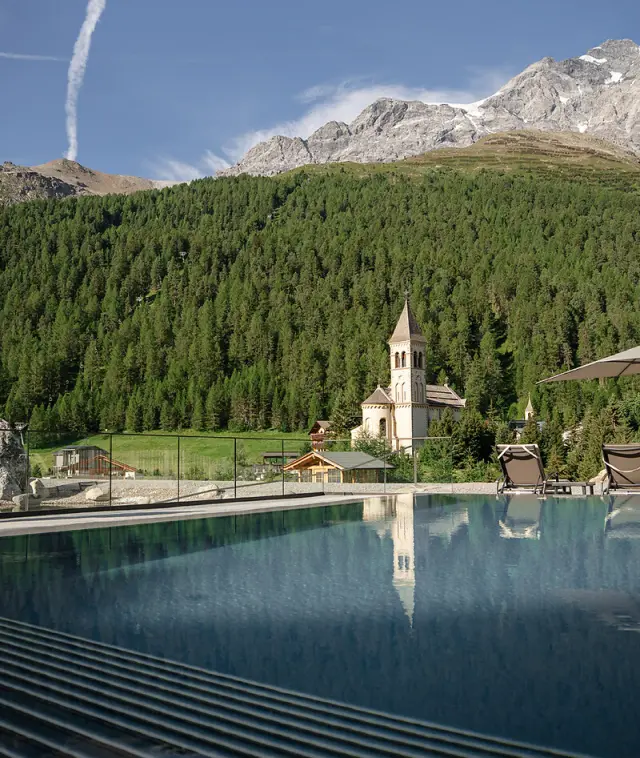 Alpin Spa Hotel die Post in Bormio – Infinity-Pool mit Blick auf Kirche und Berge | Wellnesshotel Italienische Alpen