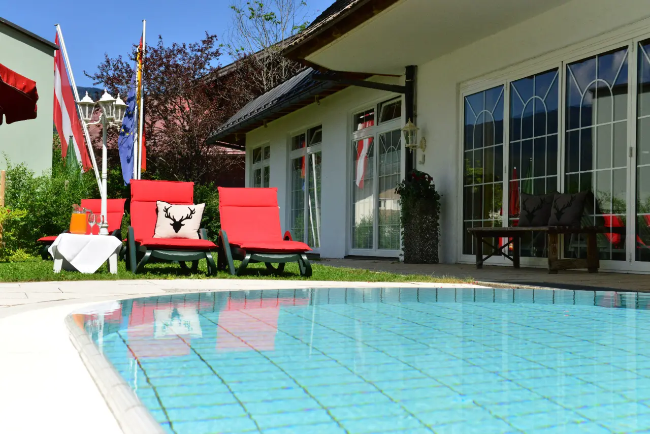 Hotel Jagdhof in Riezlern – Außenpool mit roten Liegestühlen und Hotelgebäude | Wellnesshotel Kleinwalsertal