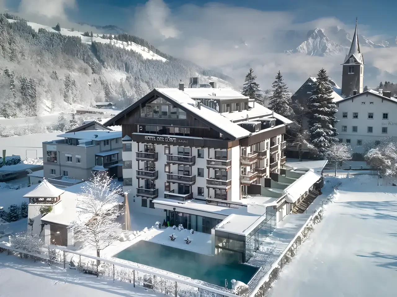 LEBE FREI Hotel DER LÖWE in Leogang – Winterliche Außenansicht mit Pool und Bergpanorama | Wellnesshotel Salzburger Land