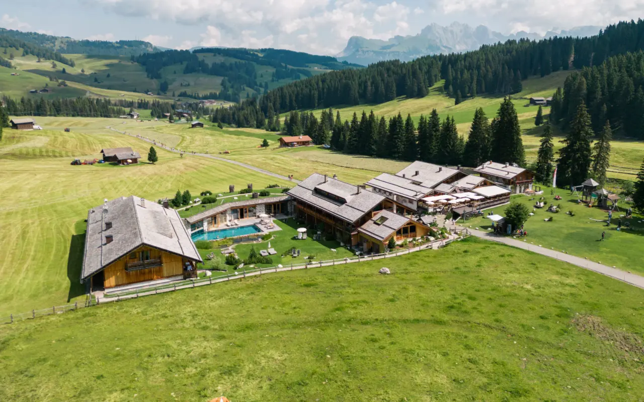 Tirler - Dolomites Living Hotel in St. Christina in Gröden – Luftaufnahme des Hotels mit Pool und Bergpanorama | Wellnesshotel Dolomiten