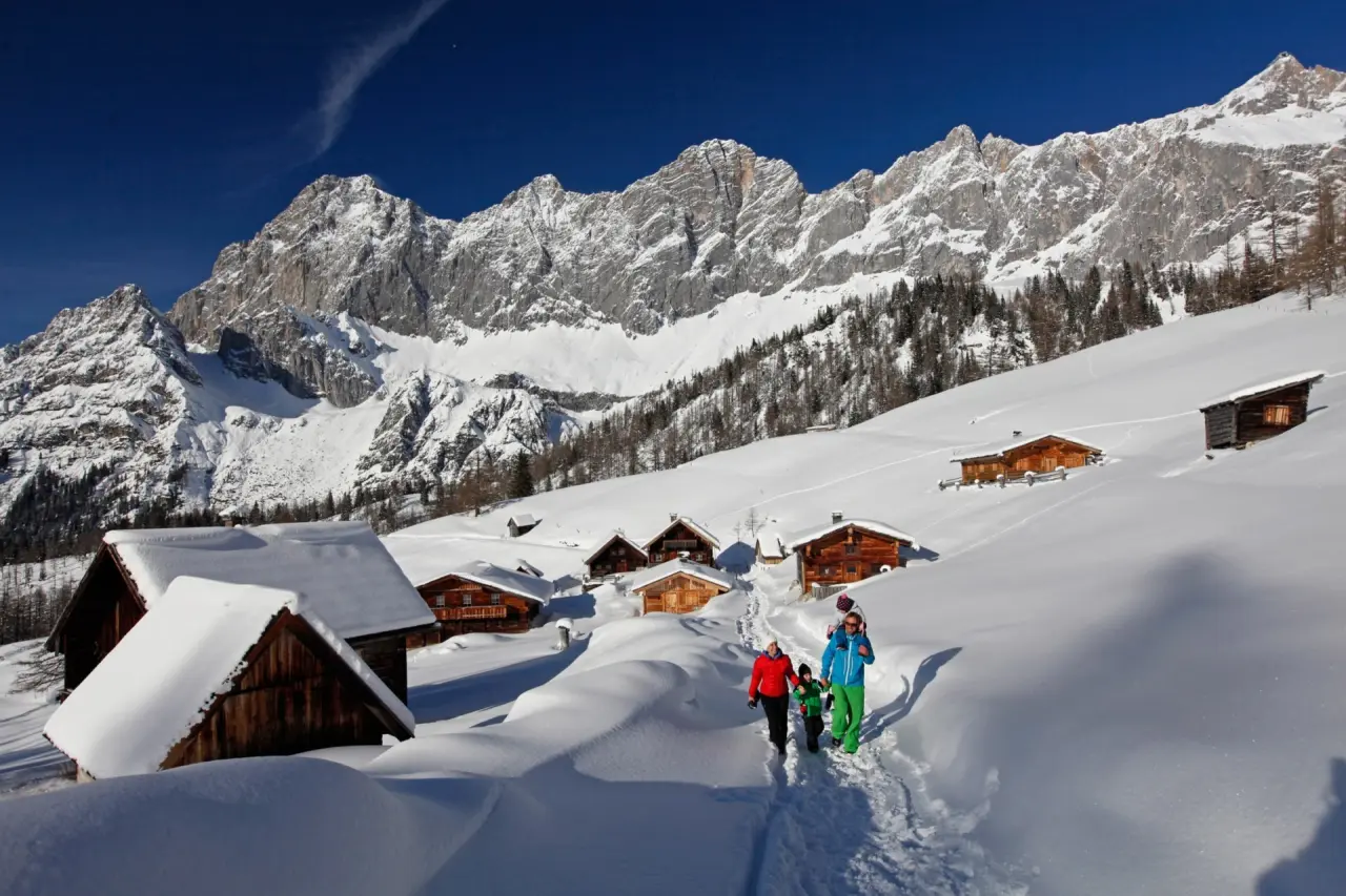 Hotel Berghof in Ramsau – Winterwanderung mit Familie vor verschneiten Berghütten und Dachsteinpanorama | Wellnesshotel Dachsteinregion