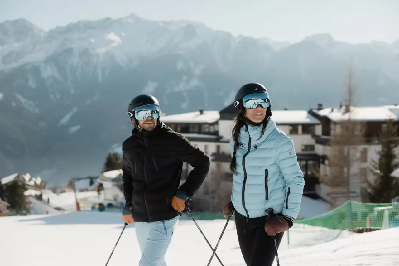 Schlosshotel Fiss in Fiss – Skifahrer-Paar vor dem Hotel mit verschneitem Bergpanorama | Wellnesshotel Tirol