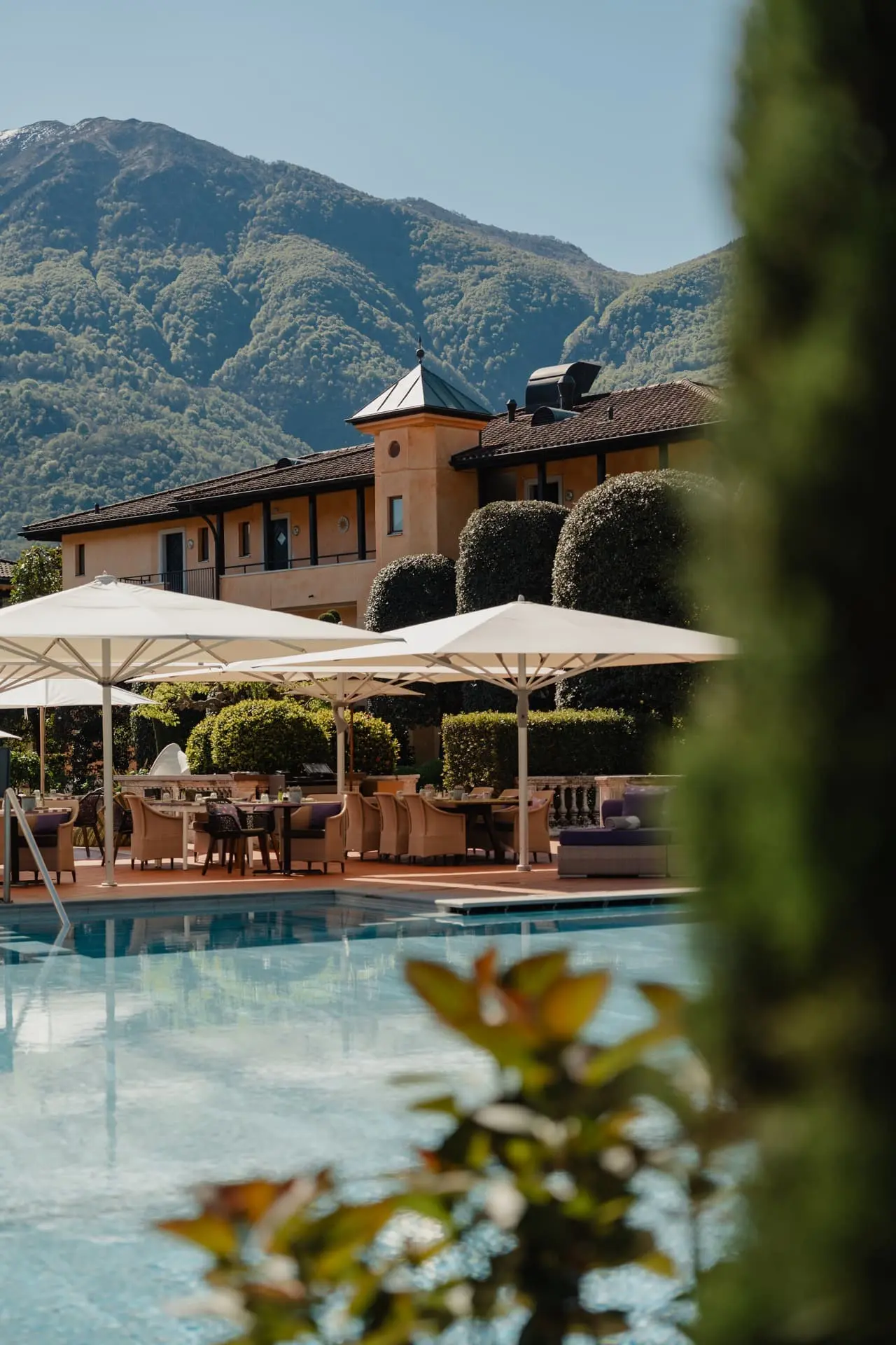 Giardino Ascona in Ascona – Außenpoolbereich mit Sonnenschirmen und Bergblick | Wellnesshotel Tessin