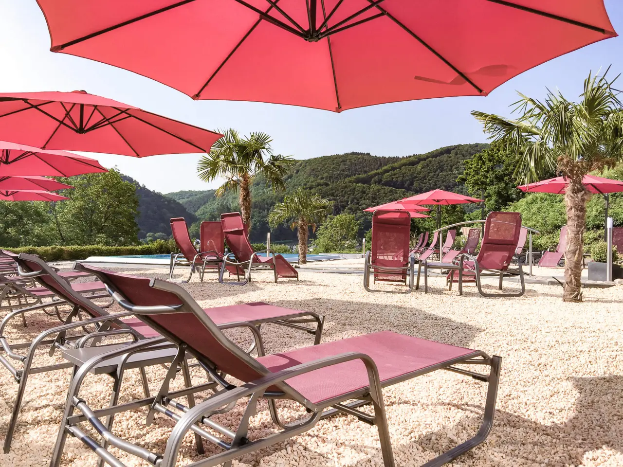 Parkhotel Krähennest in Löf – Entspannter Außenbereich mit Liegen und roten Sonnenschirmen | Wellnesshotel Mosel
