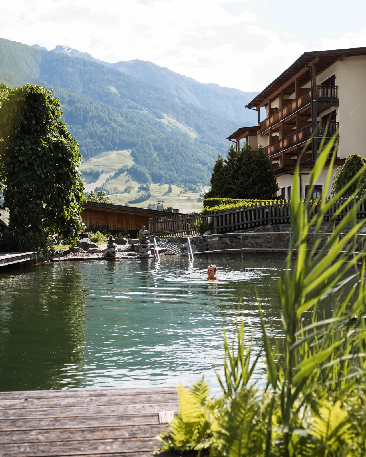 Naturhotel Outside in Matrei in Osttirol – Naturbadeteich mit Hotelgebäude und Bergpanorama | Wellnesshotel Osttirol