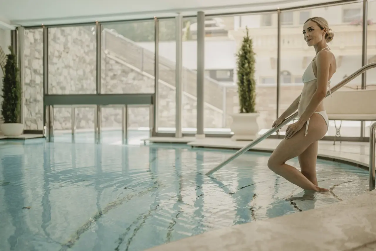 Savoy Dolomites Luxury Hotel in Wolkenstein in Gröden – Frau im Innenpool mit großen Panoramafenstern | Wellnesshotel Dolomiten