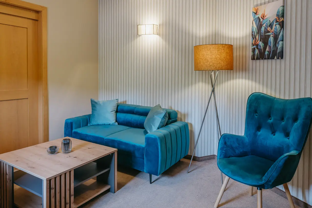 Hotel Schlafgut in Jennersdorf – Moderner Sitzbereich mit blauer Couch und Sessel im Zimmer | Wellnesshotel Jennersdorf