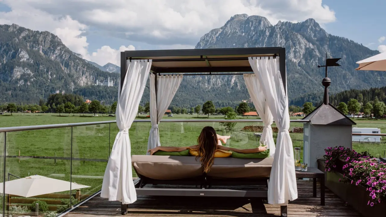 Das Rübezahl in Schwangau – Frau entspannt auf einer Daybed mit atemberaubendem Alpenblick | Wellnesshotel Allgäu