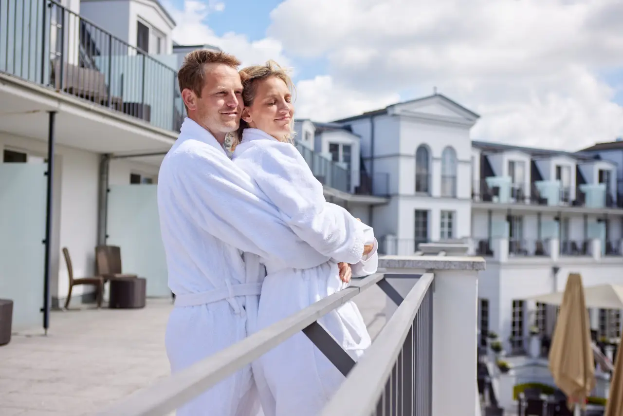 Strandhotel Zingst in Zingst – Paar in Bademänteln auf dem Balkon mit Hotelansicht | Wellnesshotel Ostsee
