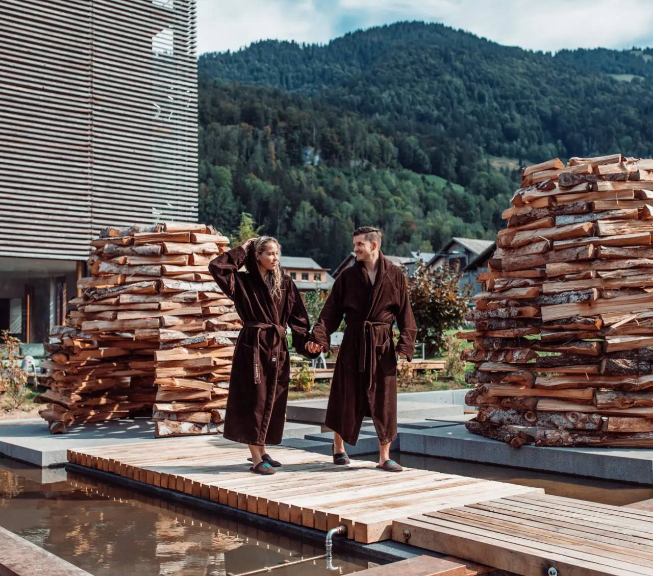 GAMS zu zweit in Bezau – Paar in Bademänteln im Außenbereich mit Holzkunst | Wellnesshotel Vorarlberg
