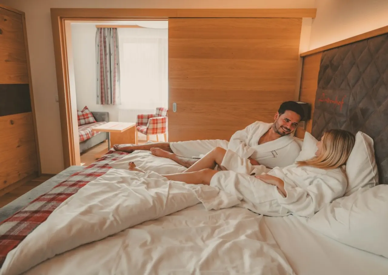 Hotel Lindenhof in Ramsau am Dachstein – Glückliches Paar entspannt im gemütlichen Hotelzimmer | Wellnesshotel Dachstein