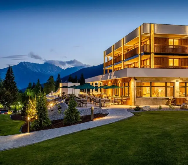 Zugspitz Resort in Ehrwald – Beleuchtete Hotelaußenansicht bei Dämmerung mit Bergpanorama | Wellnesshotel Tirol