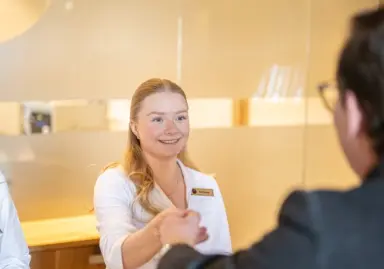 Hotel Exquisit in Oberstdorf – Freundliche Mitarbeiterin begrüßt einen Gast an der Rezeption | Wellnesshotel Allgäu