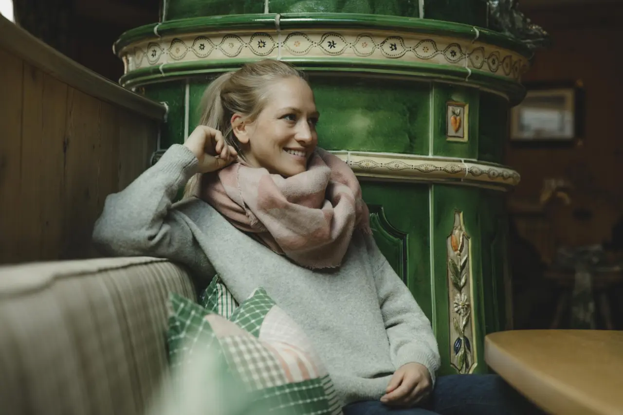 Hotel Schwarzer Adler in St. Anton am Arlberg – Entspannte Frau am Kachelofen in gemütlicher Lounge | Wellnesshotel Arlberg