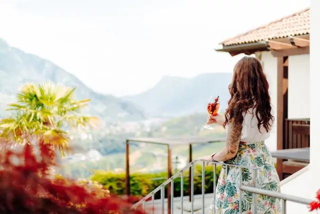 Hotel Golserhof in Tirolo – Gast genießt Bergblick vom Balkon mit Aperitif | Wellnesshotel Südtirol