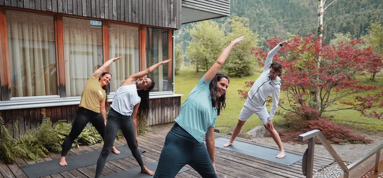 Gesundhotel Bad Reuthe****s in Reuthe – Gruppe beim Yoga auf der Holzterrasse inmitten der Natur | Wellnesshotel Bregenzerwald