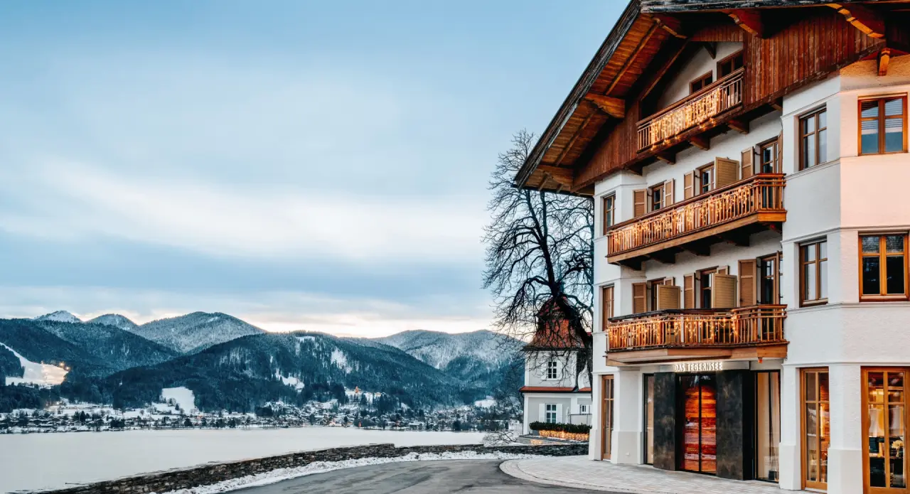 Hotel - DAS TEGERNSEE in Tegernsee – Traditionelle Hotelfassade im Winter mit Bergblick | Wellnesshotel Tegernsee