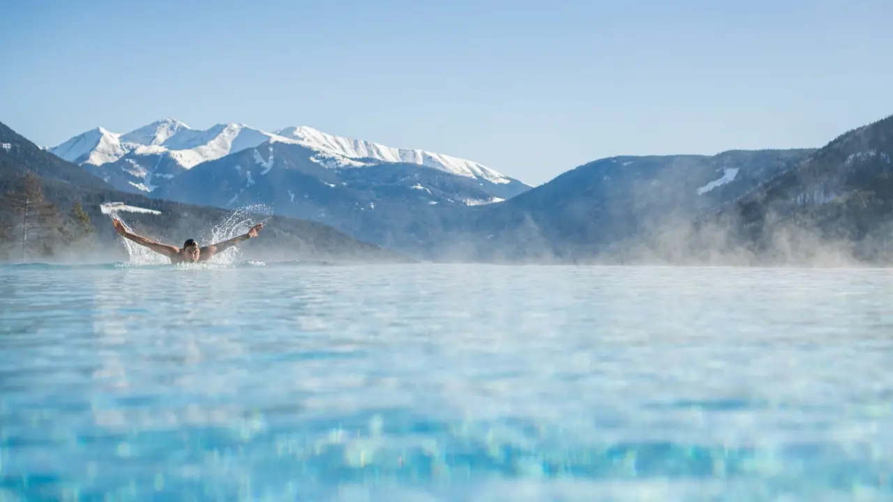 Hotel Alpen Tesitin in Toblach – Schwimmer im Infinity-Pool mit verschneiten Bergen | Wellnesshotel Südtirol