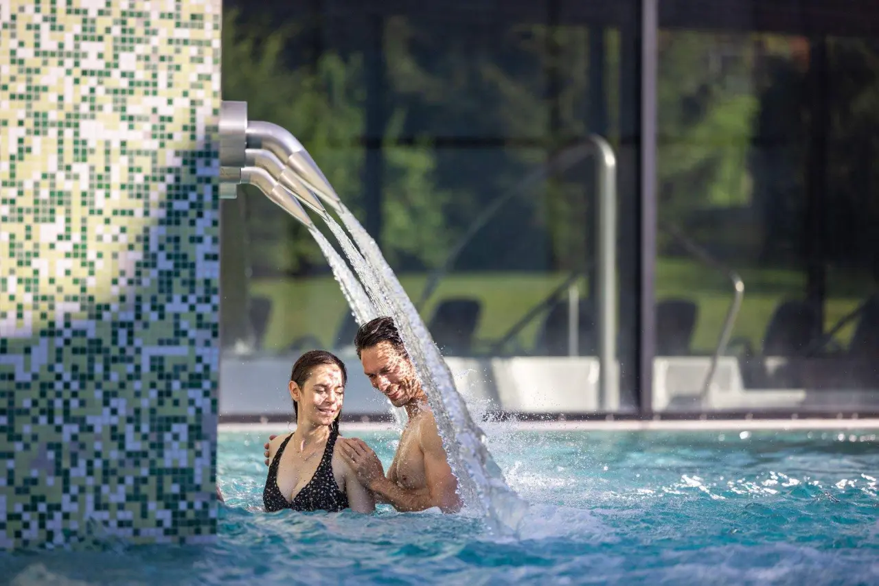 Hotel Cailler in Val-de-Charmey – Paar entspannt unter Wasserfall im Innenpool | Wellnesshotel Fribourg