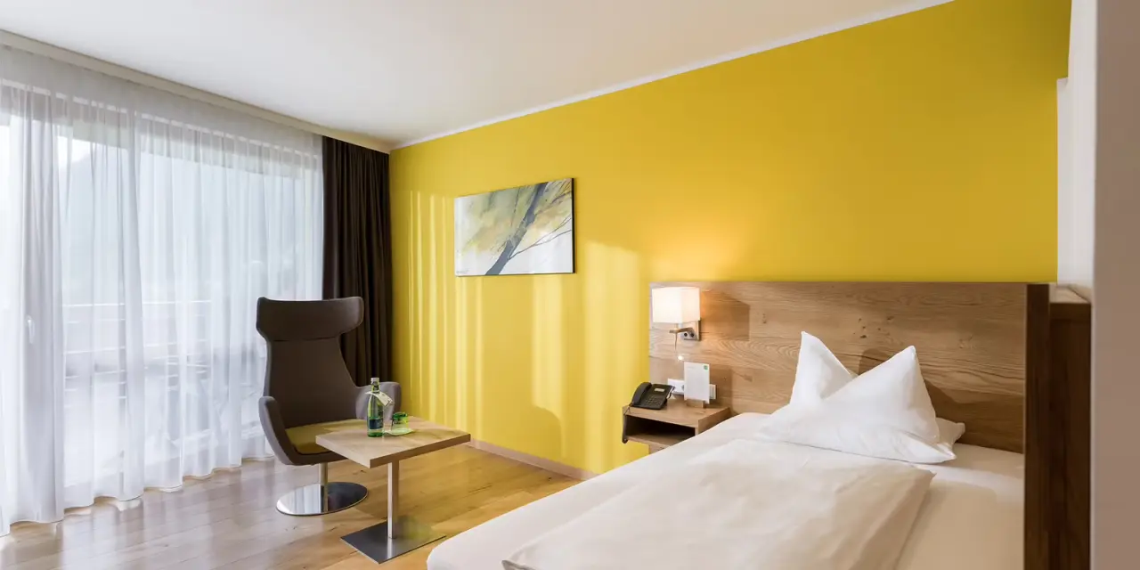 DAS SIEBEN in Bad Häring – Helles Doppelzimmer mit gelber Akzentwand und Balkon | Wellnesshotel Tirol