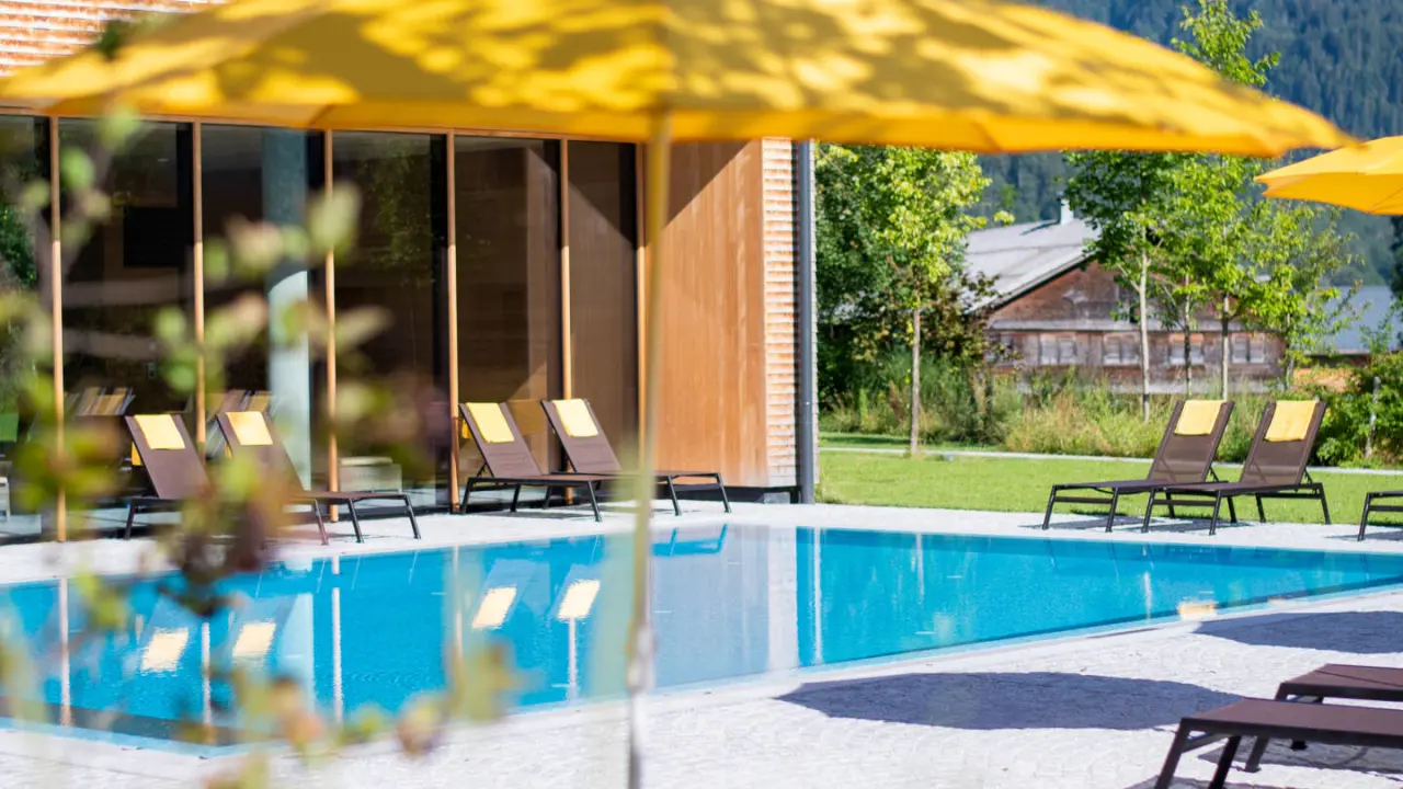 Hotel die Wälderin in Mellau – Sonniger Außenpool mit Liegen und gelben Sonnenschirmen | Wellnesshotel Bregenzerwald