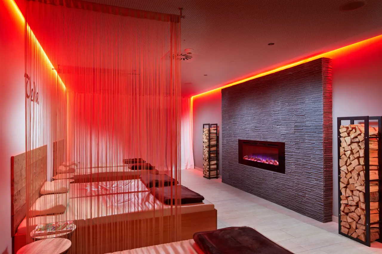 Das Alpenhaus Kaprun in Kaprun – Entspannungsraum mit Kamin und roten Lichtakzenten | Wellnesshotel Salzburger Land