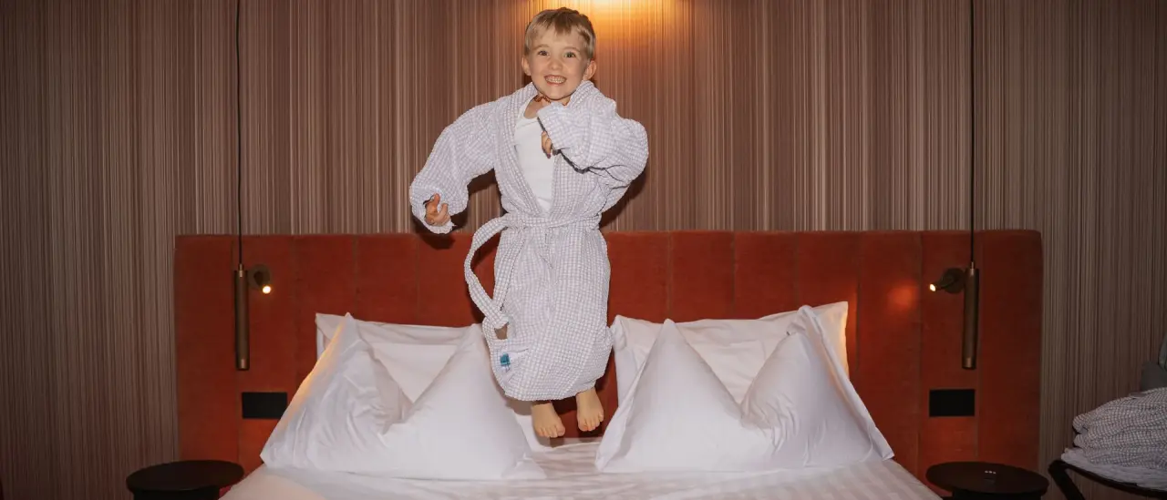 Hotel Elgus Nature Retreat in Brentonico – Kind springt fröhlich auf dem Hotelbett | Wellnesshotel Trentino