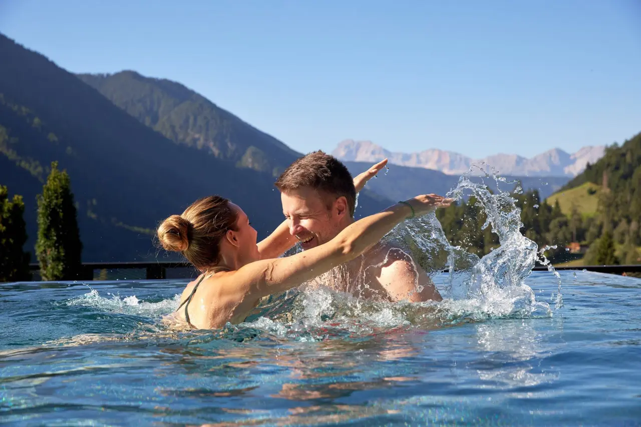 Hotel Quelle in St. Martin in Gsies – Paar hat Spaß im Infinity-Pool mit Bergpanorama | Wellnesshotel Südtirol