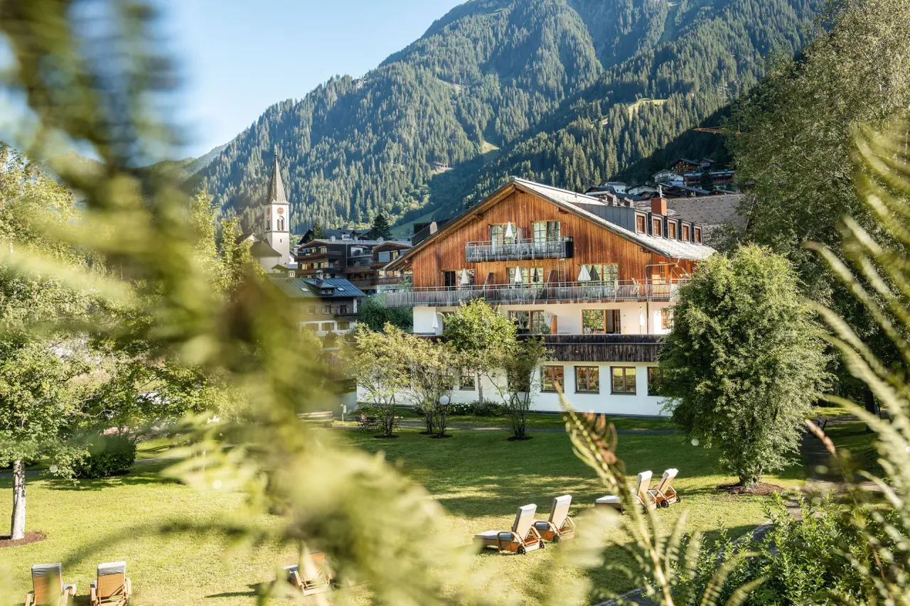 Hotel Felbermayer in Gaschurn – Sommeransicht des Hotels mit gepflegtem Garten und Dorfkirche | Wellnesshotel Montafon