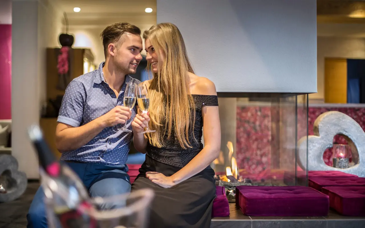 mein romantisches Hotel Garni Toalstock in Fiss – Romantisches Paar mit Sekt vor einem Kamin im Hotel | Wellnesshotel Tirol