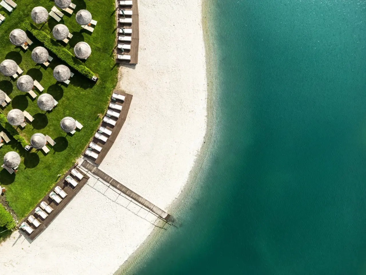 St. Martins Therme & Lodge in Frauenkirchen – Strandbereich mit Liegen und Sonnenschirmen am See | Wellnesshotel Burgenland