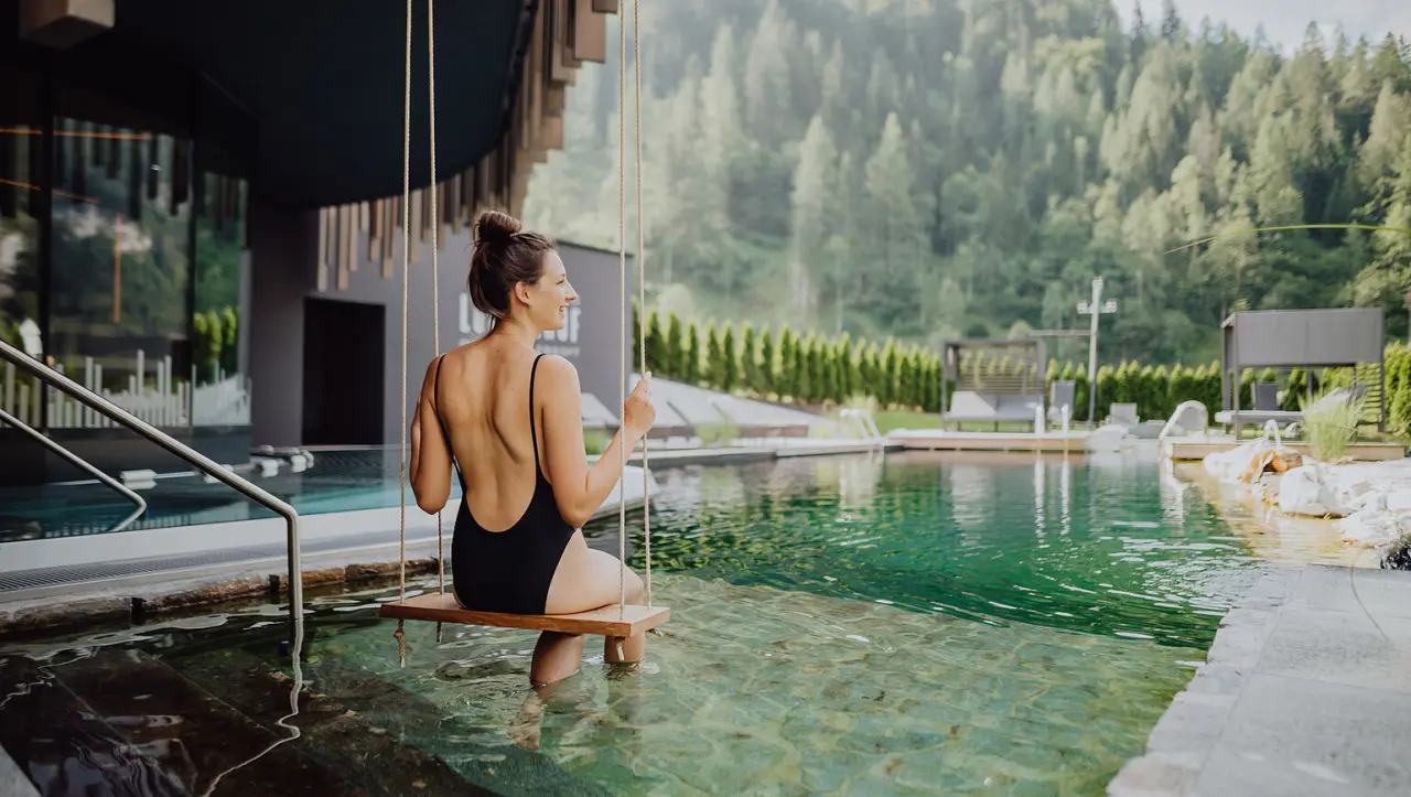 Alpin Life Resort Lürzerhof in Untertauern – Frau auf Wasserschaukel im Außenpool mit Bergblick | Wellnesshotel Salzburger Land