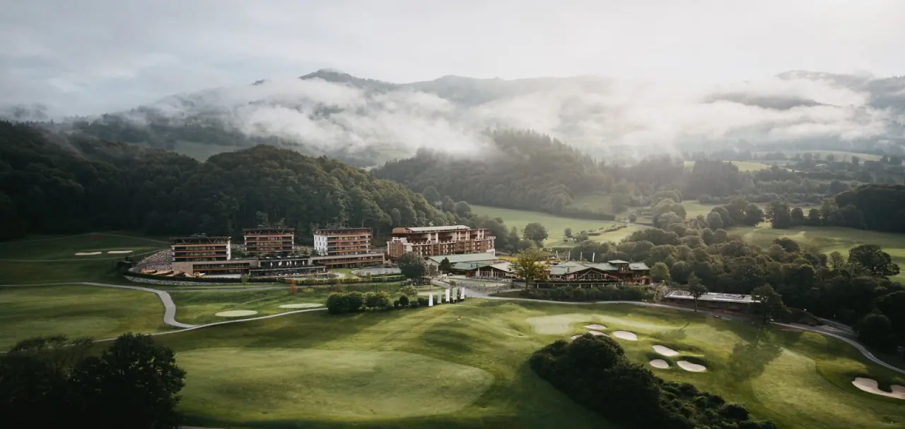 Grand Tirolia Kitzbühel in Kitzbühel – Luftaufnahme des Hotels mit Golfplatz und Nebel | Wellnesshotel Tirol