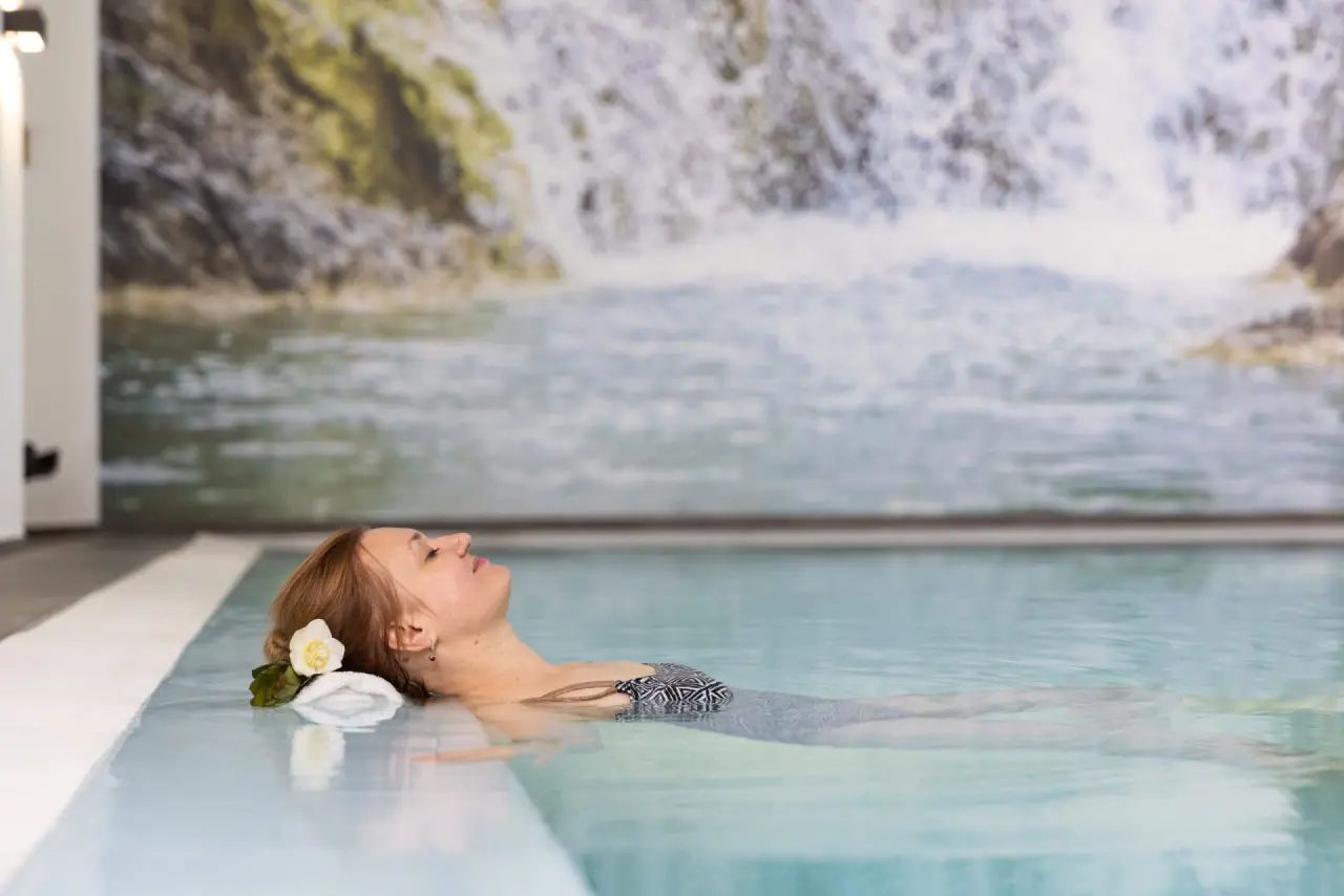 Tanneck Golf & Spa in Bad Wörishofen – Frau entspannt im Innenpool mit Wasserfall-Wandbild | Wellnesshotel Allgäu