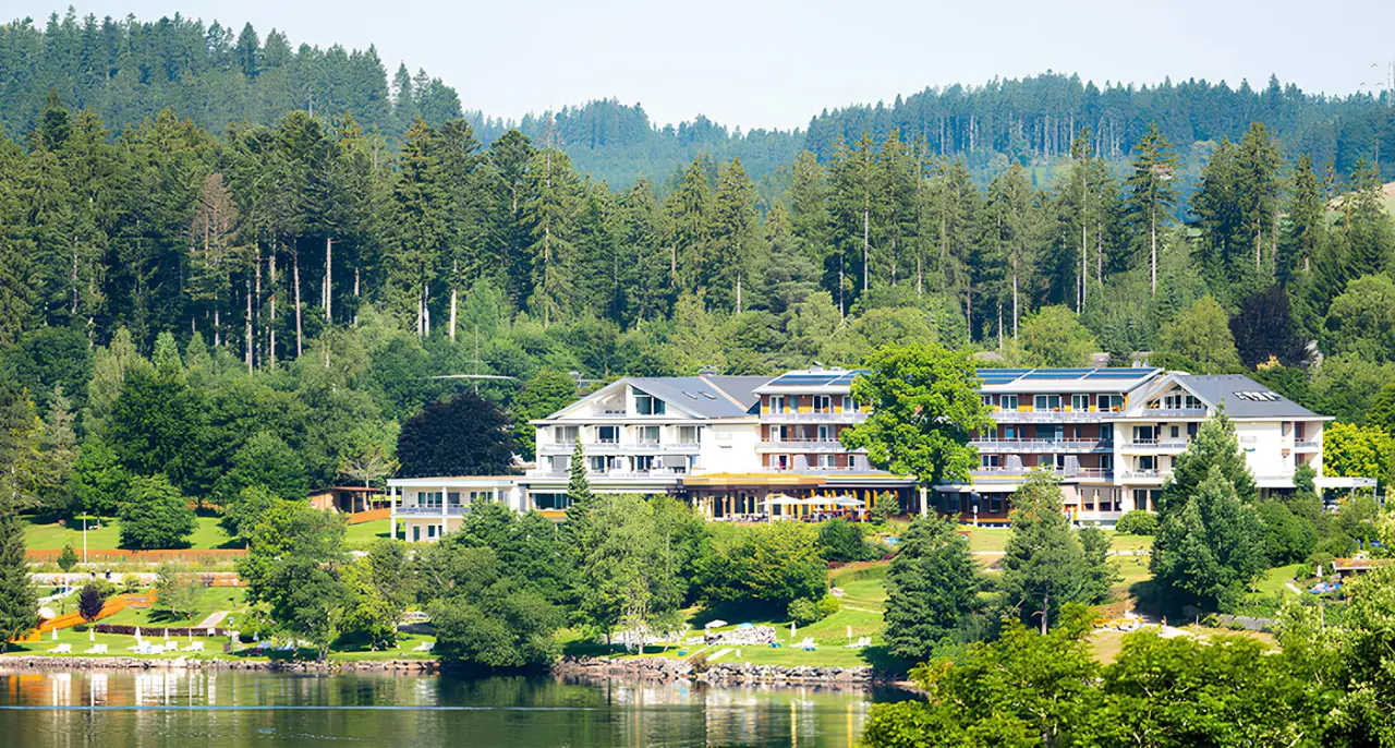 Brugger's Hotelpark am Titisee in Titisee – Hotelansicht vom Seeufer mit Waldkulisse | Wellnesshotel Schwarzwald